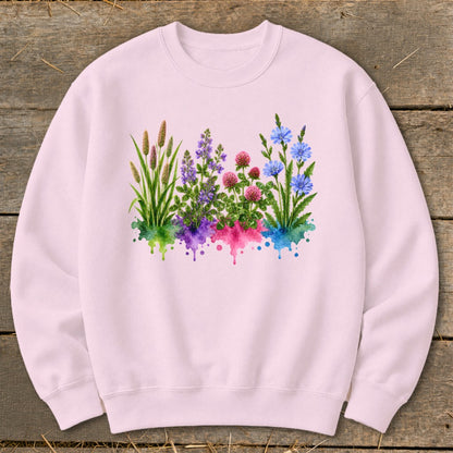 A light pink crewneck sweatshirt features a central graphic of watercolor wildflowers springing from colorful splatters.