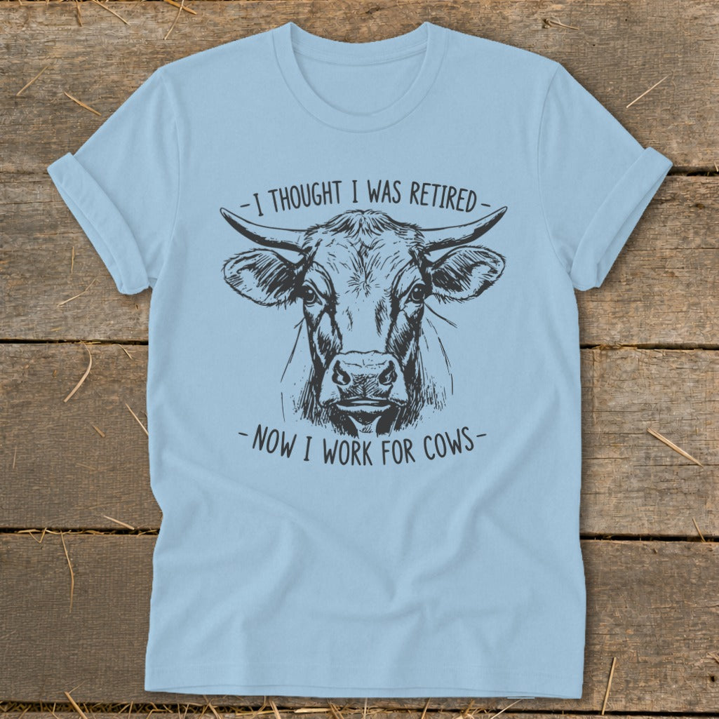 Light blue t-shirt with a sketch of a cow and text "I THOUGHT I WAS RETIRED - NOW I WORK FOR COWS".