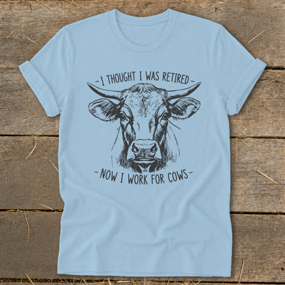 Light blue t-shirt with a sketch of a cow and text "I THOUGHT I WAS RETIRED - NOW I WORK FOR COWS".