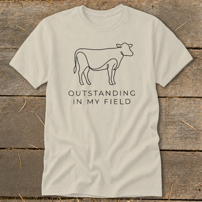 Light beige t-shirt with line art cow and "OUTSTANDING IN MY FIELD" text.