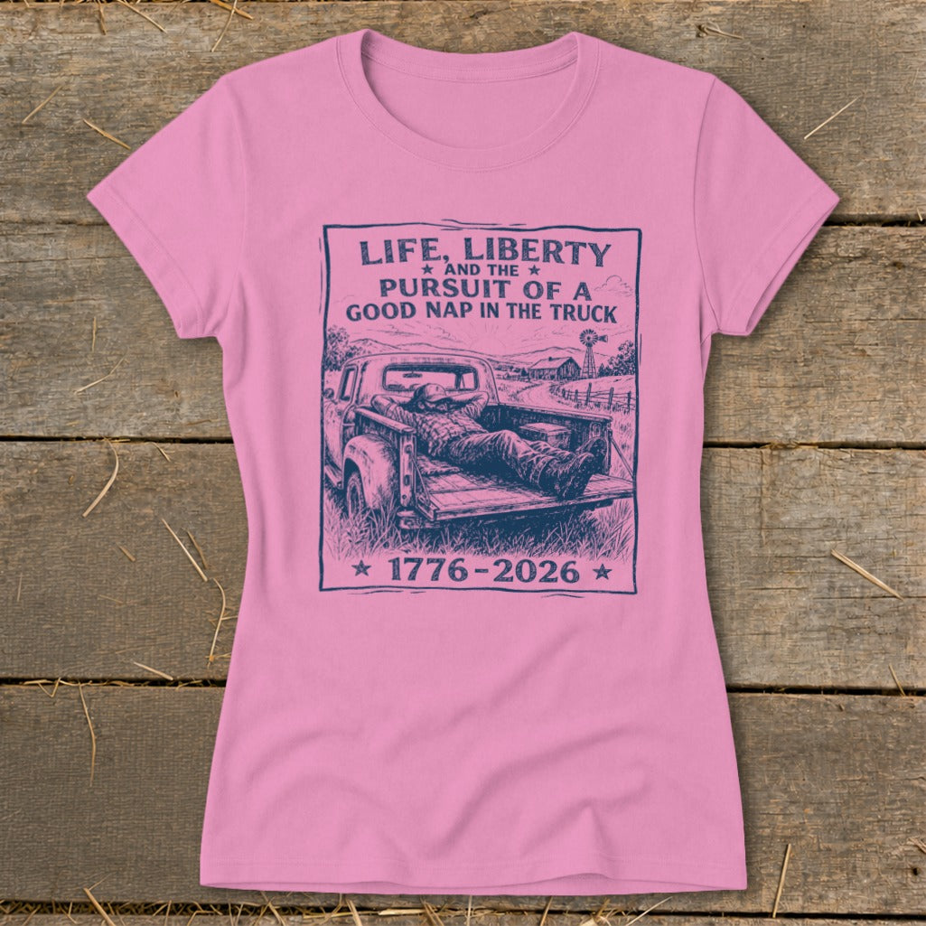 Pink t-shirt with graphic of man sleeping in truck bed, reading "Life, Liberty, and the Pursuit of a Good Nap in the Truck".
