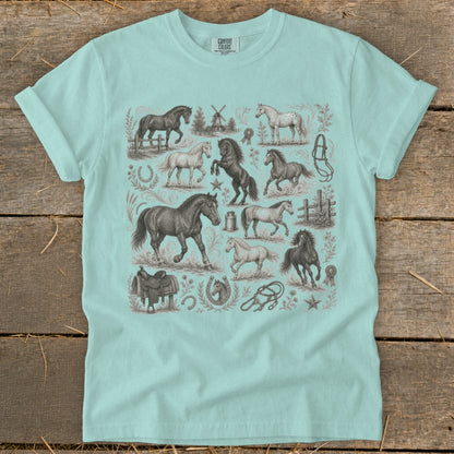 Light blue t-shirt with a repeating graphic of horses, saddles, horseshoes, and a windmill.