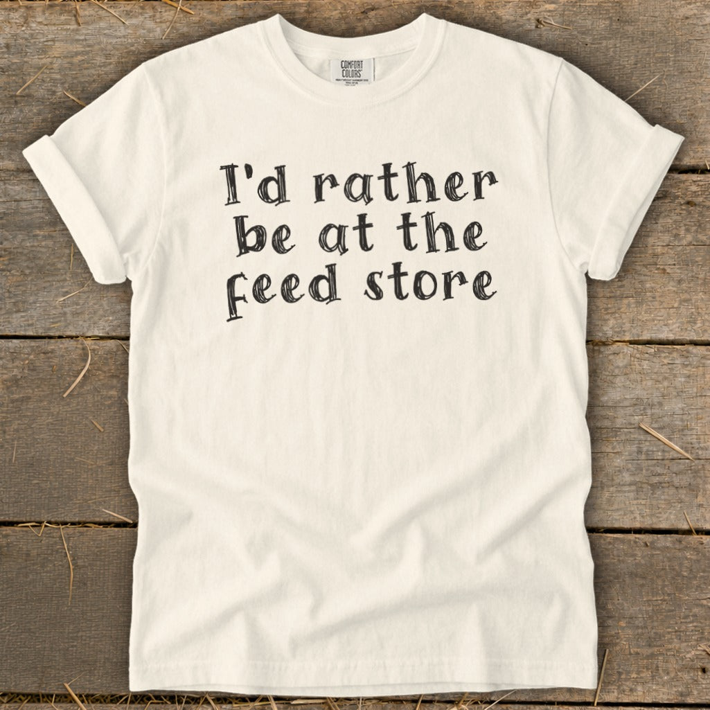 Cream t-shirt with black text that reads "I'd rather be at the feed store."