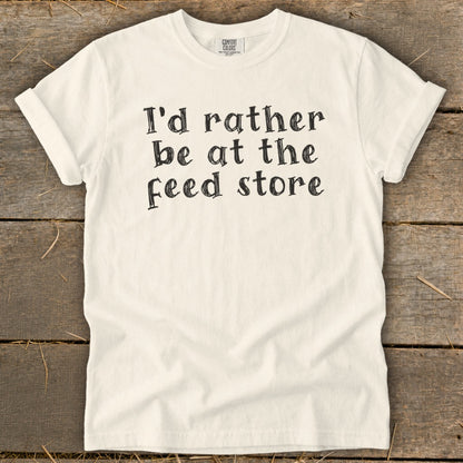 Cream t-shirt with black text that reads "I'd rather be at the feed store."