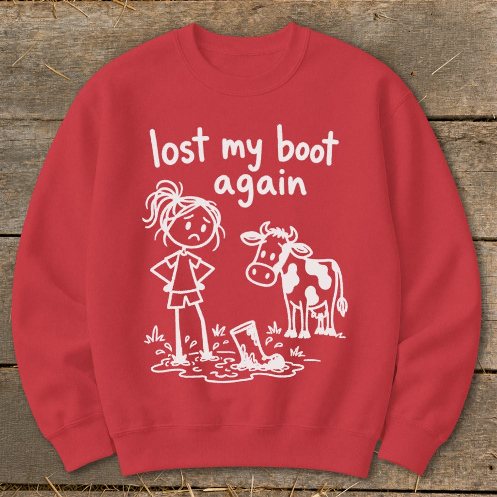 Red crewneck sweatshirt featuring a white graphic of a sad stick figure girl, a cow, and a lost boot in a mud puddle, with the text "lost my boot again."