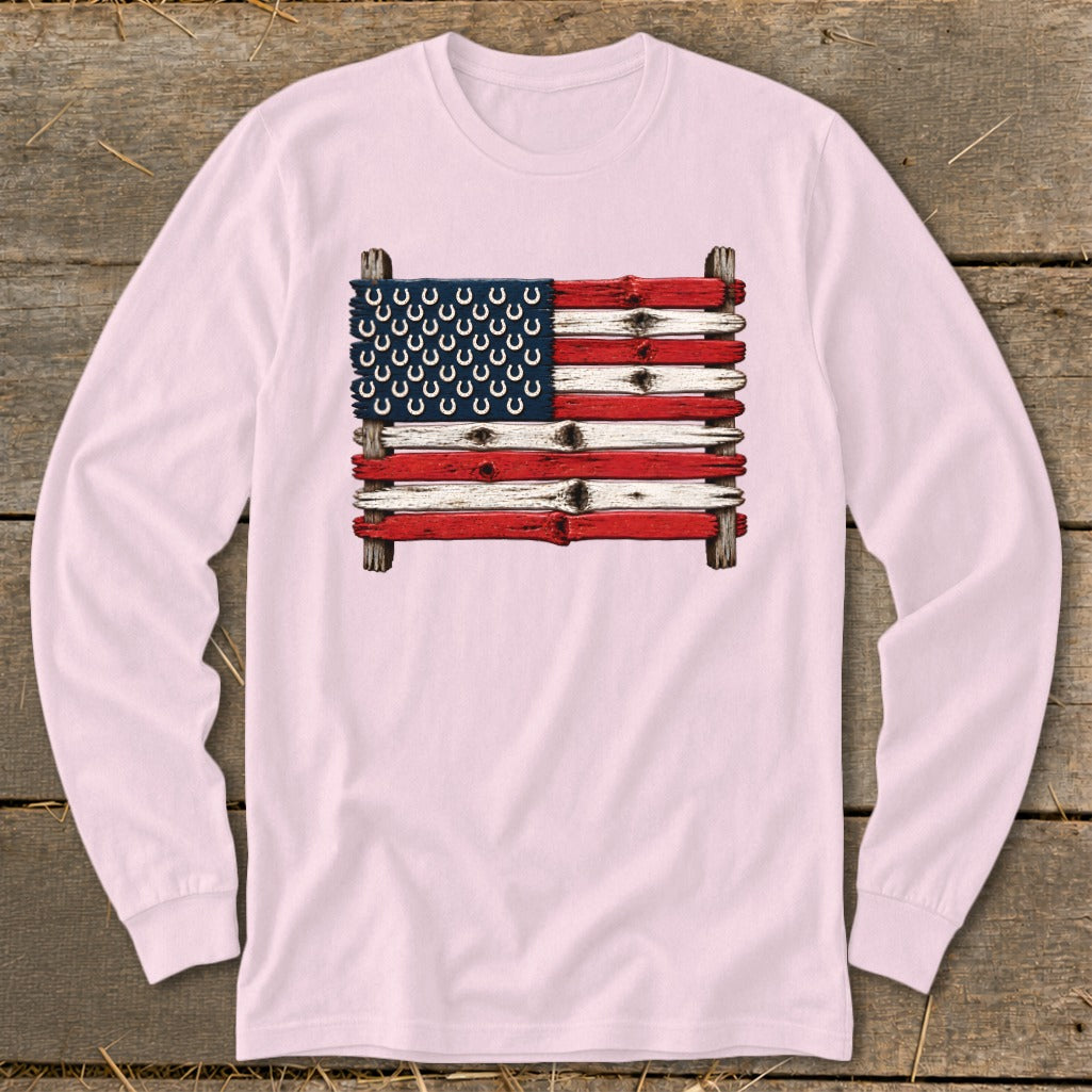 Light pink long-sleeve t-shirt featuring a rustic American flag graphic made of painted wooden boards and horseshoes.