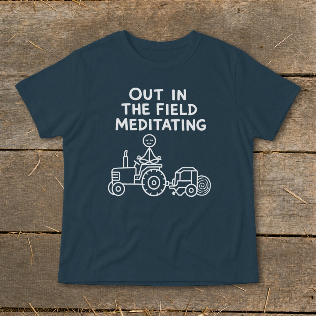 Navy t-shirt with white text "OUT IN THE FIELD MEDITATING" and a stick figure meditating on a tractor.