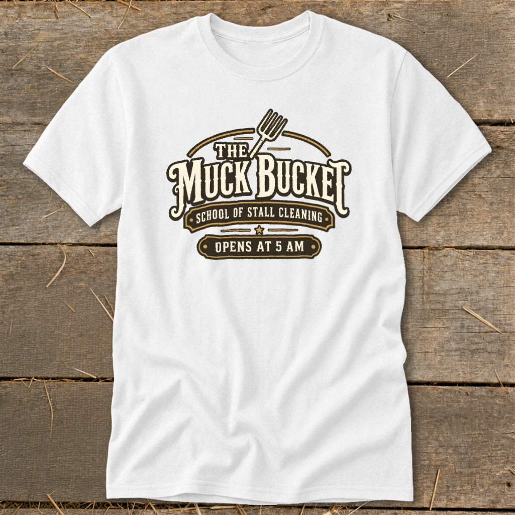 White t-shirt with "The Muck Bucket School of Stall Cleaning Opens at 5 AM" logo.