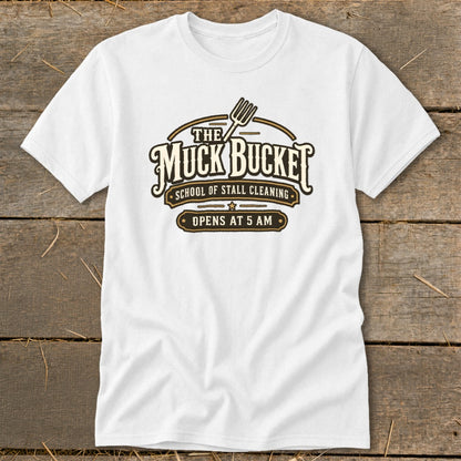 White t-shirt with "The Muck Bucket School of Stall Cleaning Opens at 5 AM" logo.
