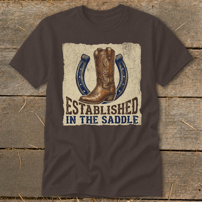 Brown t-shirt with cowboy boot, horseshoes, and text "ESTABLISHED IN THE SADDLE".