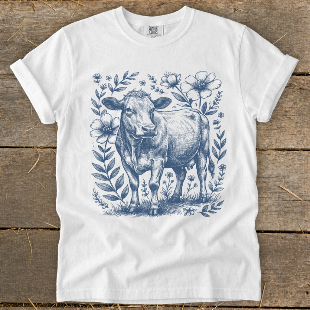 White t-shirt with blue sketch of a cow surrounded by flowers and leaves.