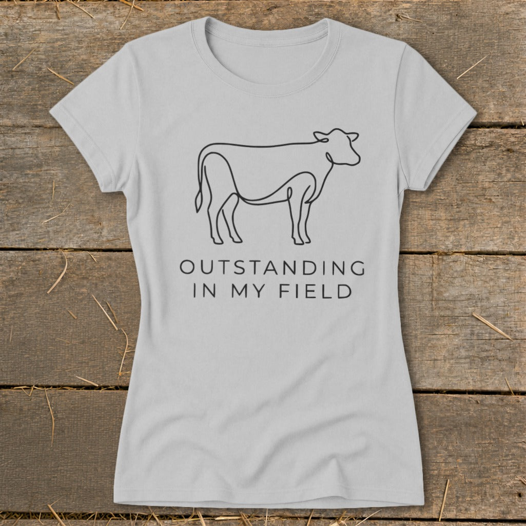 Light gray t-shirt with black line art cow and text "OUTSTANDING IN MY FIELD".