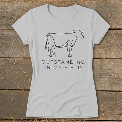 Light gray t-shirt with black line art cow and text "OUTSTANDING IN MY FIELD".