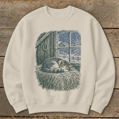 Cream sweatshirt with a drawing of a sleeping cat on hay by a snowy window.