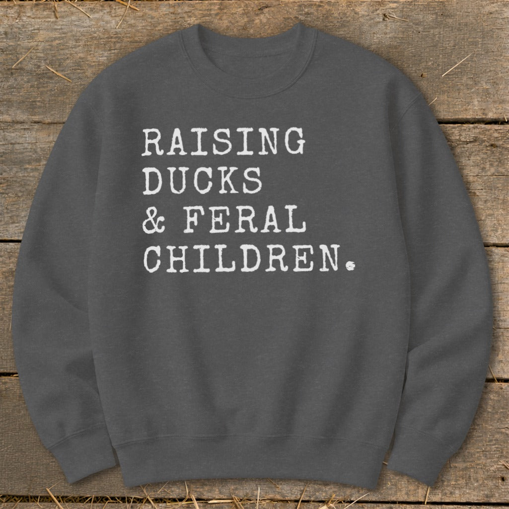 Dark grey sweatshirt with white text reading "RAISING DUCKS & FERAL CHILDREN."