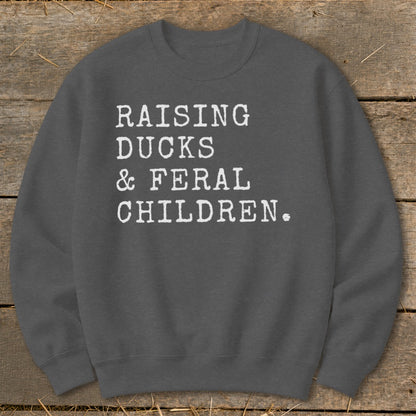 Dark grey sweatshirt with white text reading "RAISING DUCKS & FERAL CHILDREN."
