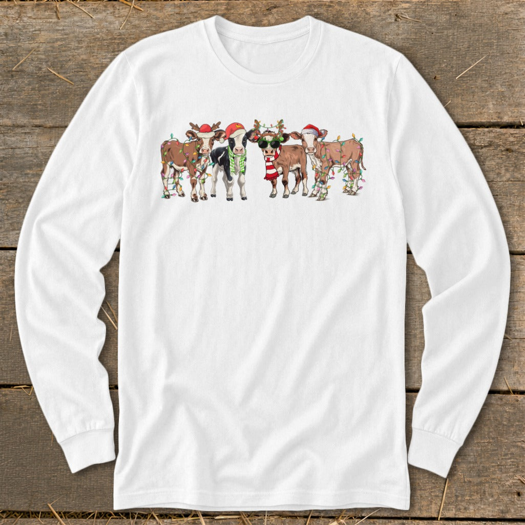 Five cartoon cows wear Santa hats and festive lights on a white long-sleeve shirt.