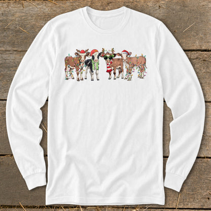 Five cartoon cows wear Santa hats and festive lights on a white long-sleeve shirt.