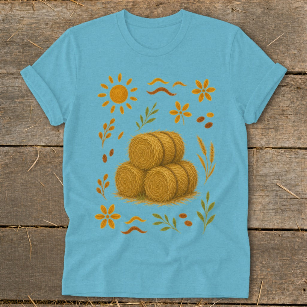Light blue t-shirt with hay bale graphic, sun, flowers, and leaves.