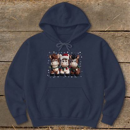 Three cartoon horses in Christmas attire stand with snowflakes on a navy hoodie.