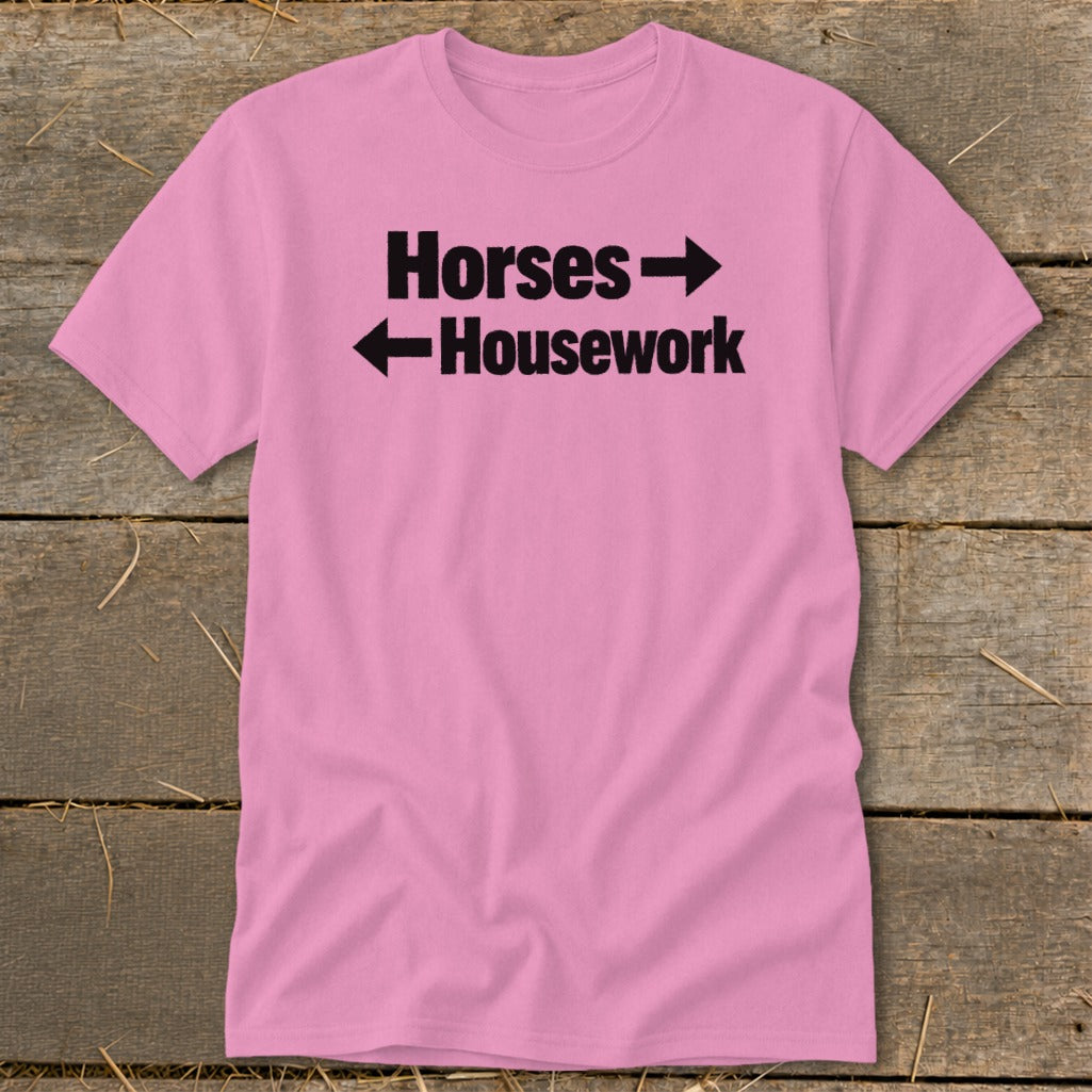 A pink t-shirt with black text that reads Horses with a right arrow above Housework with a left arrow.