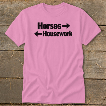 A pink t-shirt with black text that reads Horses with a right arrow above Housework with a left arrow.