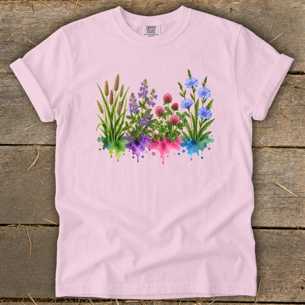 A light pink t-shirt featuring a watercolor botanical print of wildflowers over colorful paint splatters.