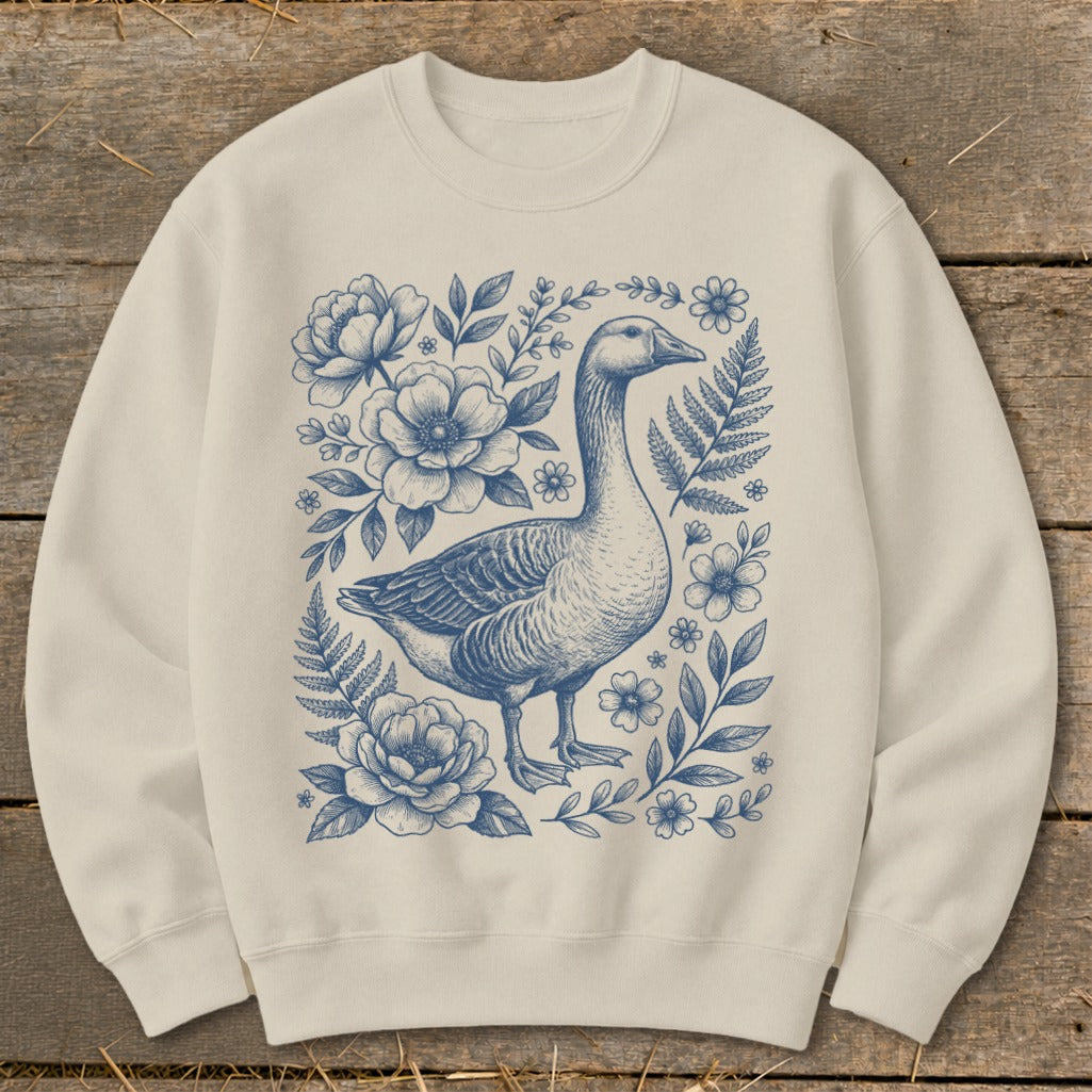Cream sweatshirt with a blue ink drawing of a goose surrounded by flowers and ferns.