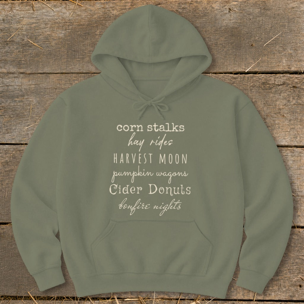 Olive green hoodie with list of fall activities: corn stalks, hay rides, harvest moon, pumpkin wagons, cider donuts, bonfire nights.