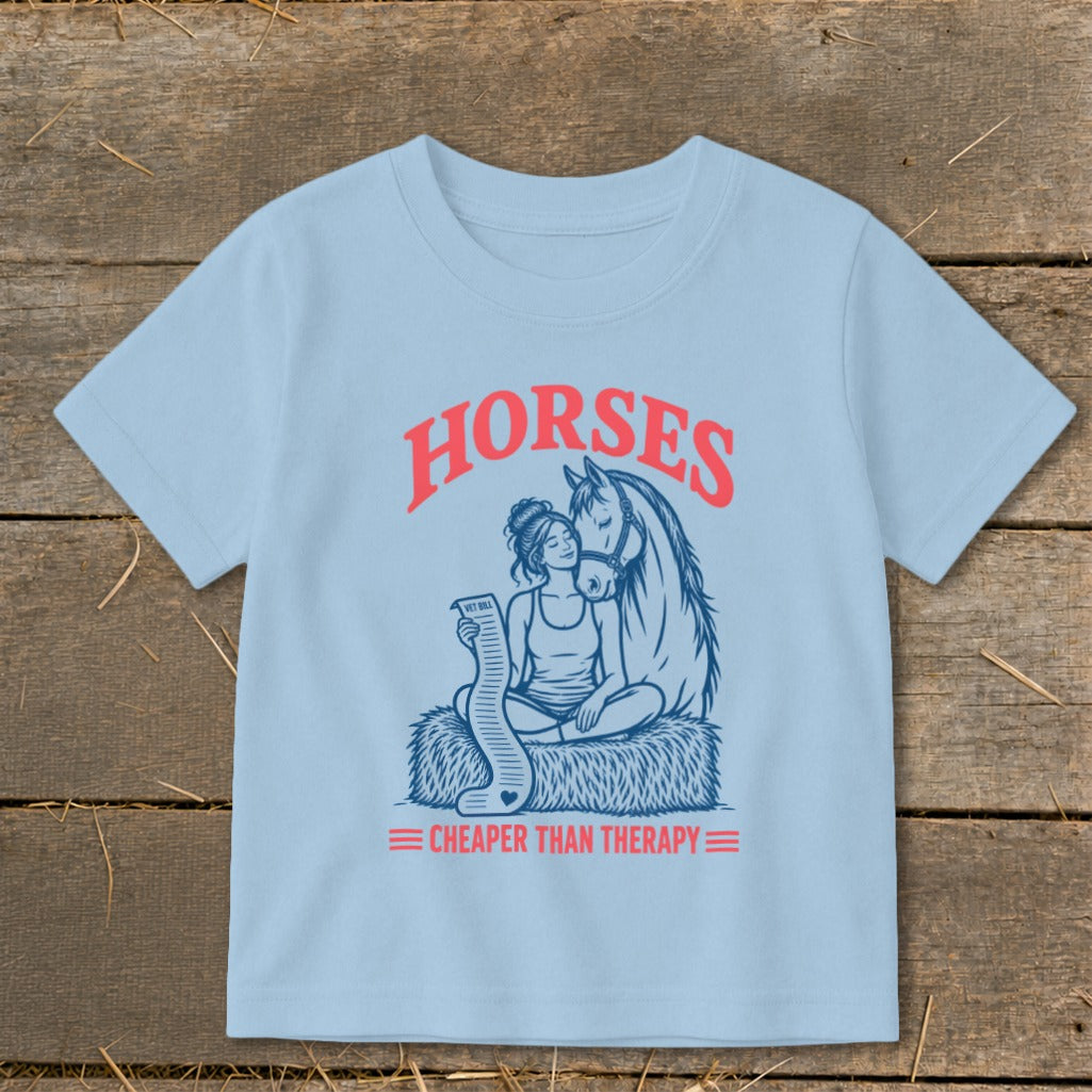 Light blue t-shirt graphic with "HORSES CHEAPER THAN THERAPY" and a woman with a horse holding a vet bill.