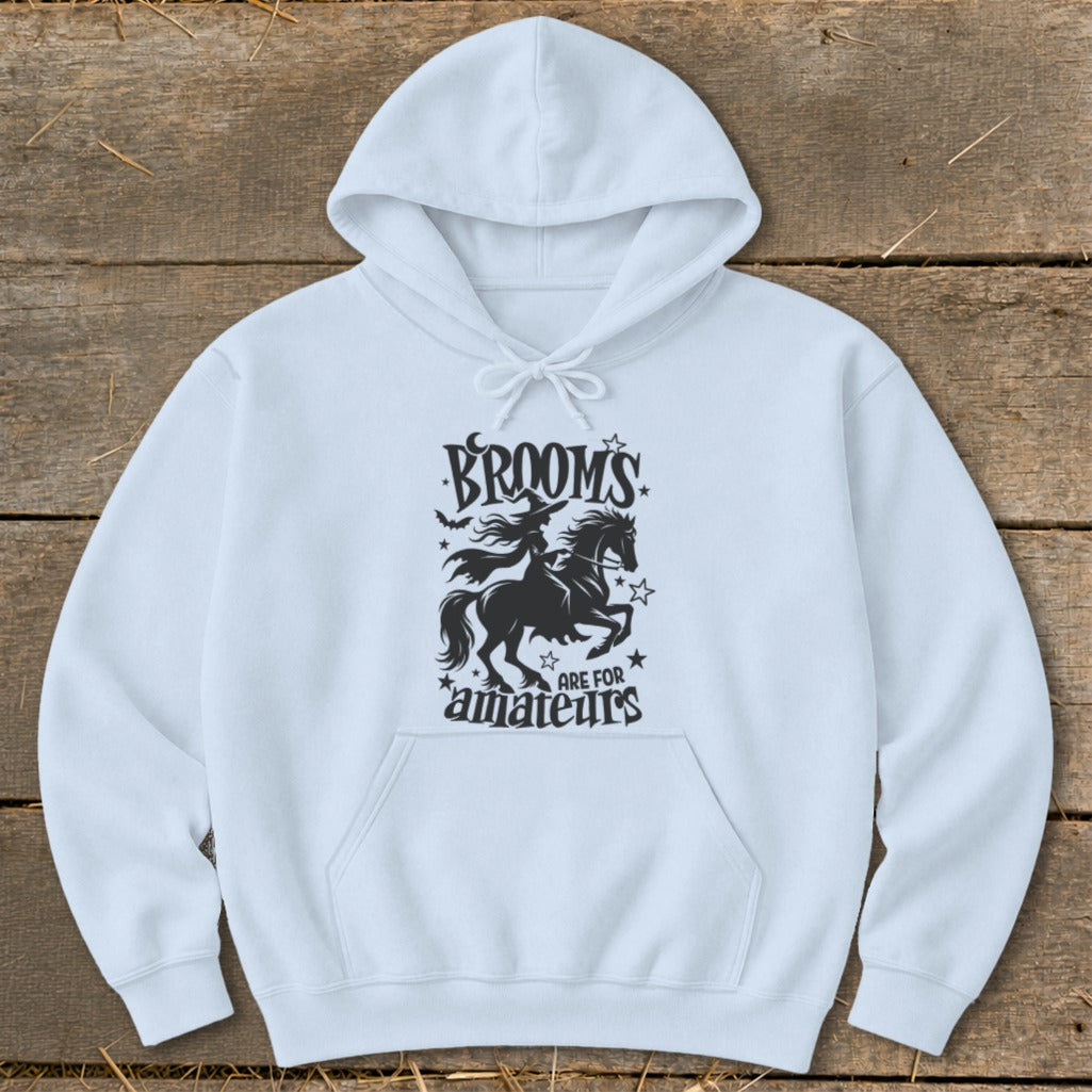 White hoodie with black graphic of witch on a horse, text reads "BROOMS ARE FOR AMATEURS".
