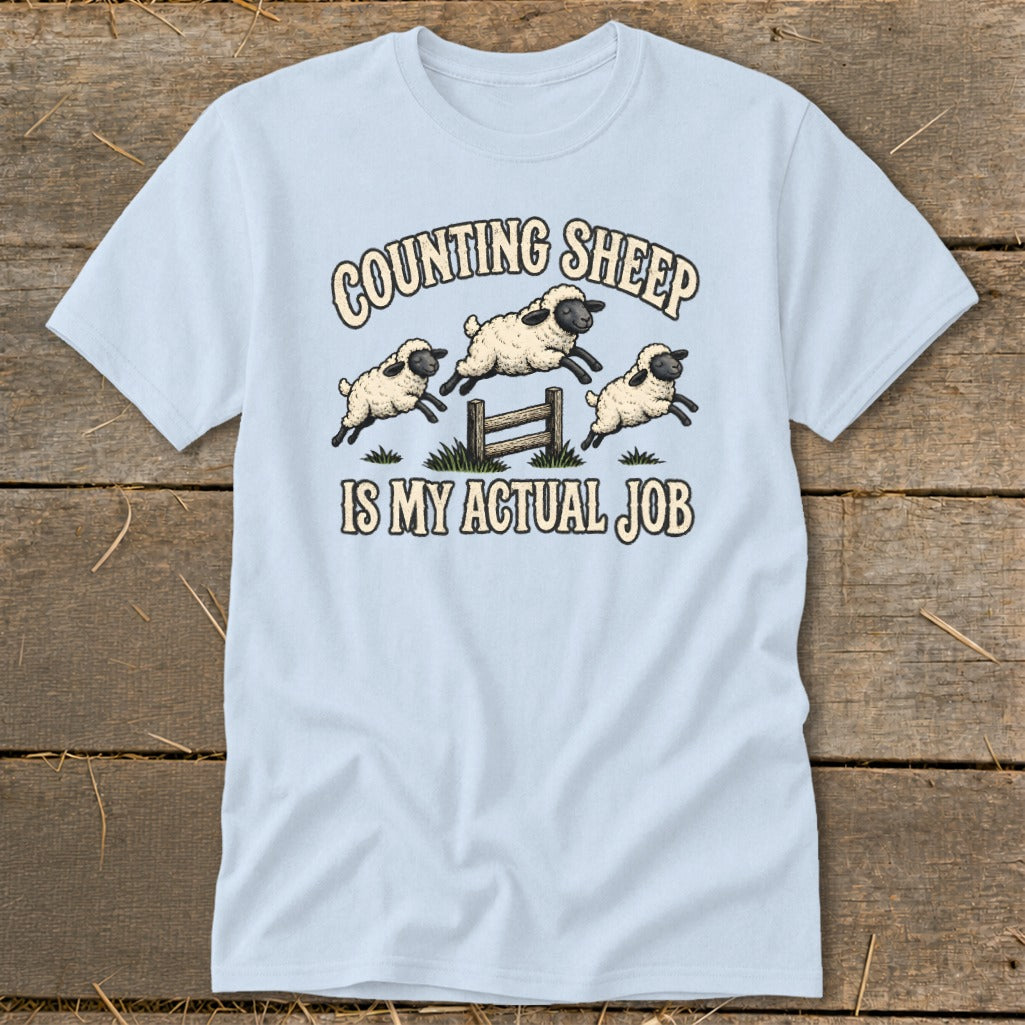 Light blue t-shirt with cartoon sheep jumping over a fence and text "Counting Sheep Is My Actual Job".