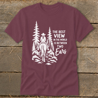 Maroon t-shirt with a white graphic of a horseback rider among pine trees and text reading The best view in the world is between two ears.