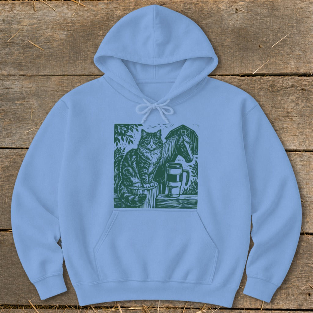 Light blue hoodie with a green linocut design of a cat, horse, and mug.