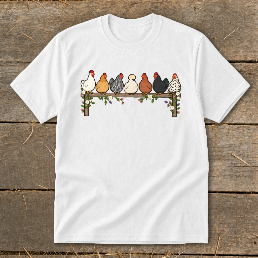 White t-shirt featuring an illustration of seven colorful chickens perched on a flower-decorated wooden fence.