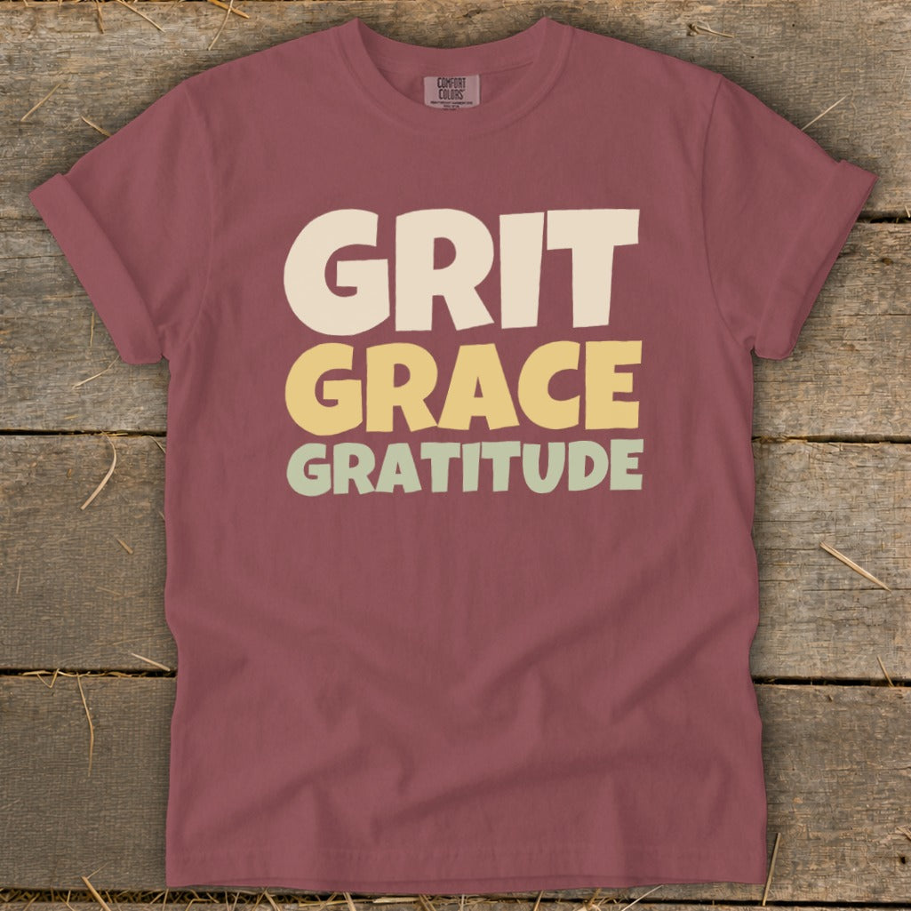 A mauve crewneck t-shirt with the words Grit, Grace, and Gratitude printed in stacked, block lettering.