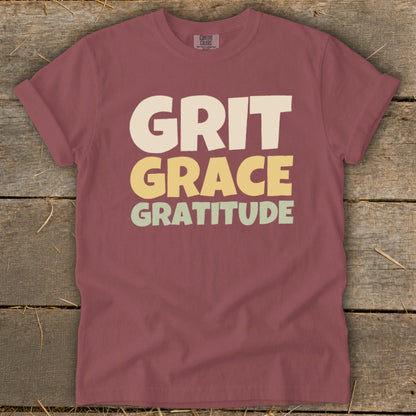 A mauve crewneck t-shirt with the words Grit, Grace, and Gratitude printed in stacked, block lettering.