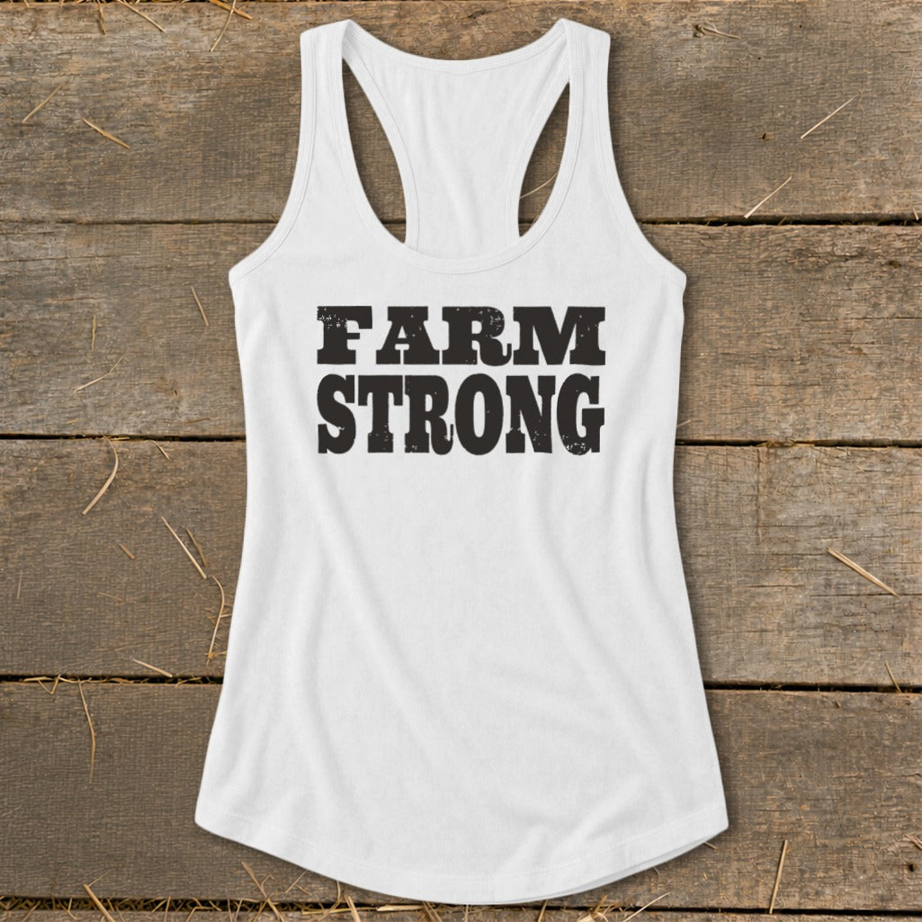 White racerback tank top with distressed black Farm Strong text laid flat on weathered wood.