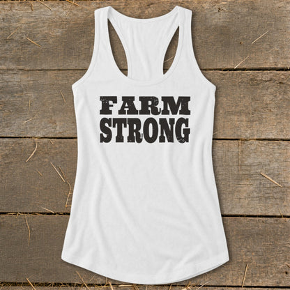 White racerback tank top with distressed black Farm Strong text laid flat on weathered wood.