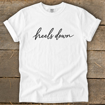 White t-shirt with "heels down" in black cursive text.