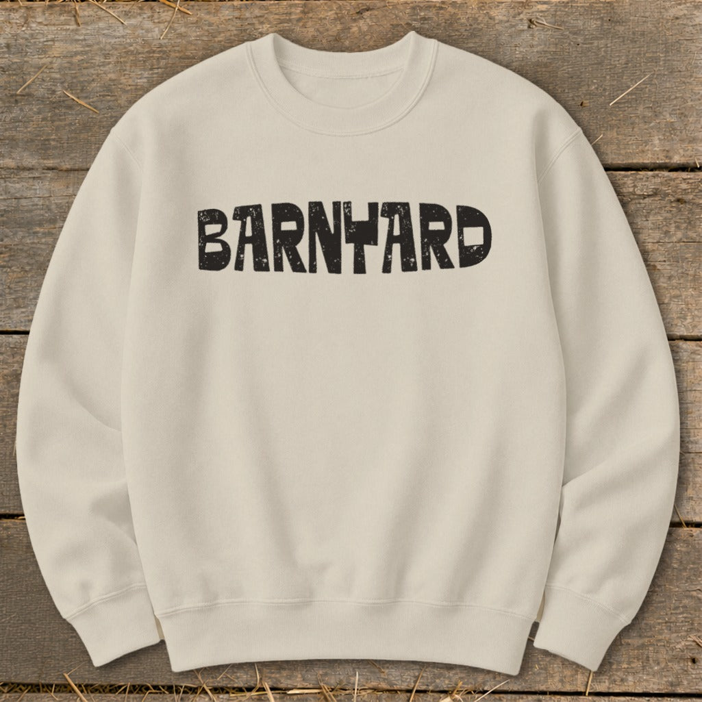 Off-white crewneck sweatshirt featuring the black distressed text BARNYARD centered on the chest, laid flat on a rustic wooden background.