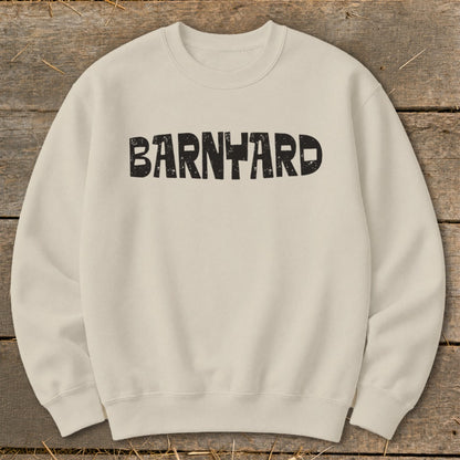 Off-white crewneck sweatshirt featuring the black distressed text BARNYARD centered on the chest, laid flat on a rustic wooden background.