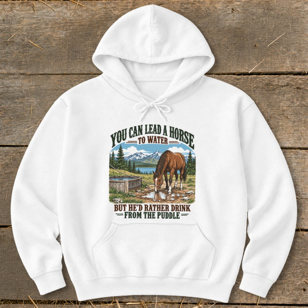 A white hooded sweatshirt with graphic text reading You can lead a horse to water but he d rather drink from the puddle above an illustration of a horse drinking from a puddle.