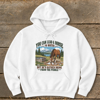 A white hooded sweatshirt with graphic text reading You can lead a horse to water but he d rather drink from the puddle above an illustration of a horse drinking from a puddle.