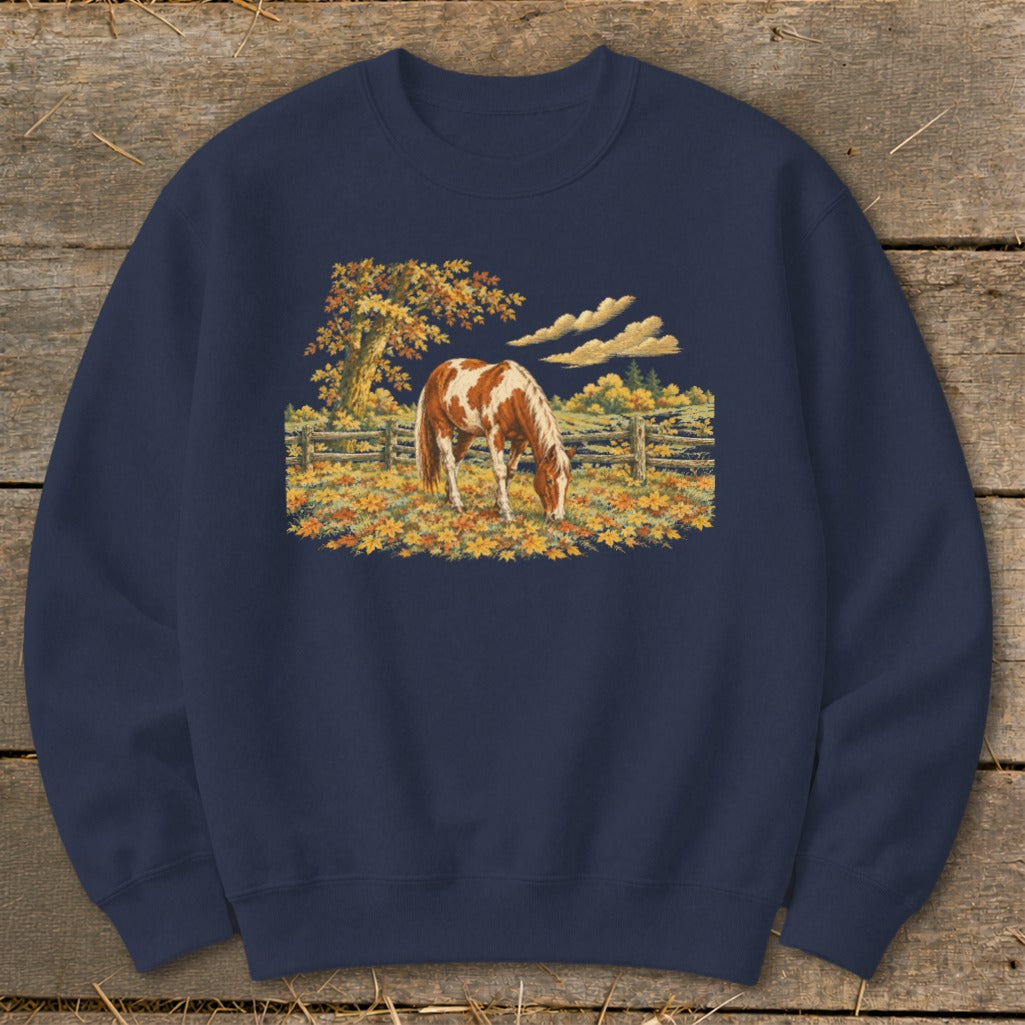 Brown and white horse grazing in a field of autumn leaves with a tree and fence.