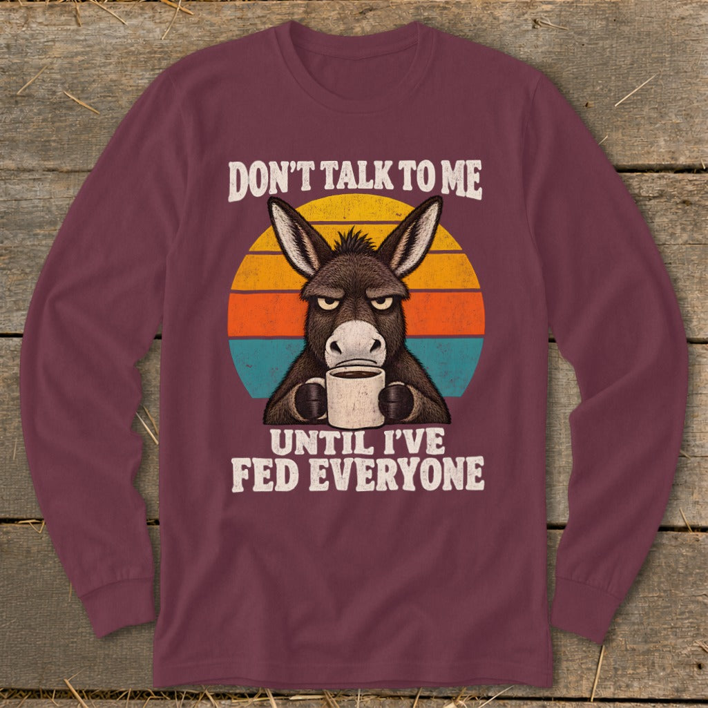 Maroon long-sleeve shirt featuring a grumpy donkey holding a coffee mug against a retro sunset graphic.