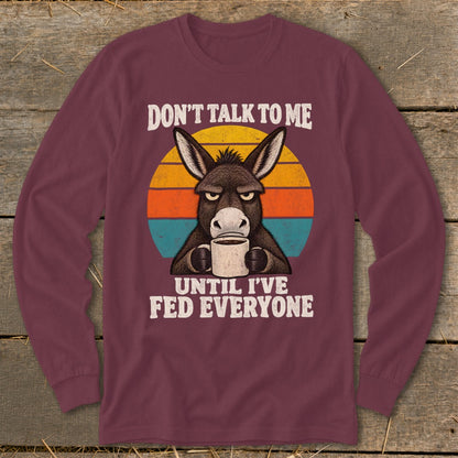Maroon long-sleeve shirt featuring a grumpy donkey holding a coffee mug against a retro sunset graphic.