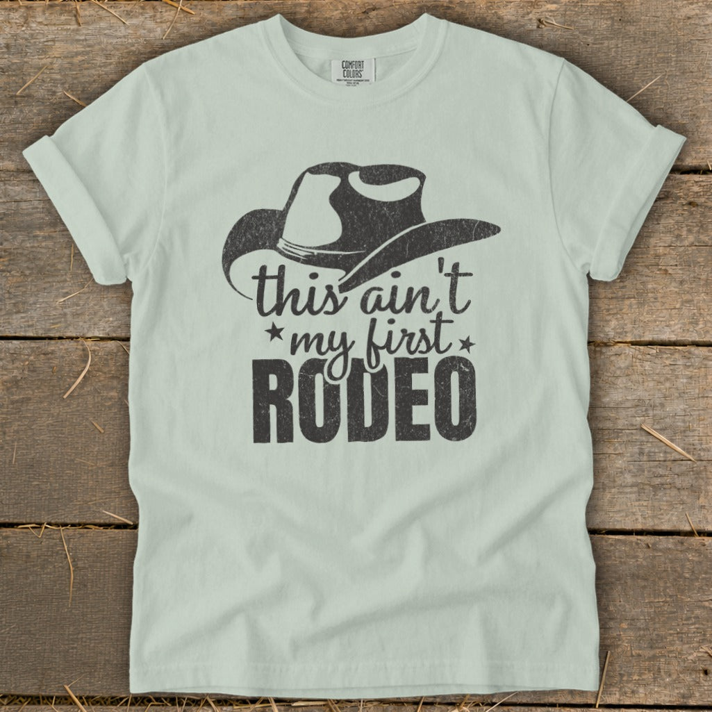 Light blue t-shirt with a distressed cowboy hat graphic and "this ain't my first RODEO" text.