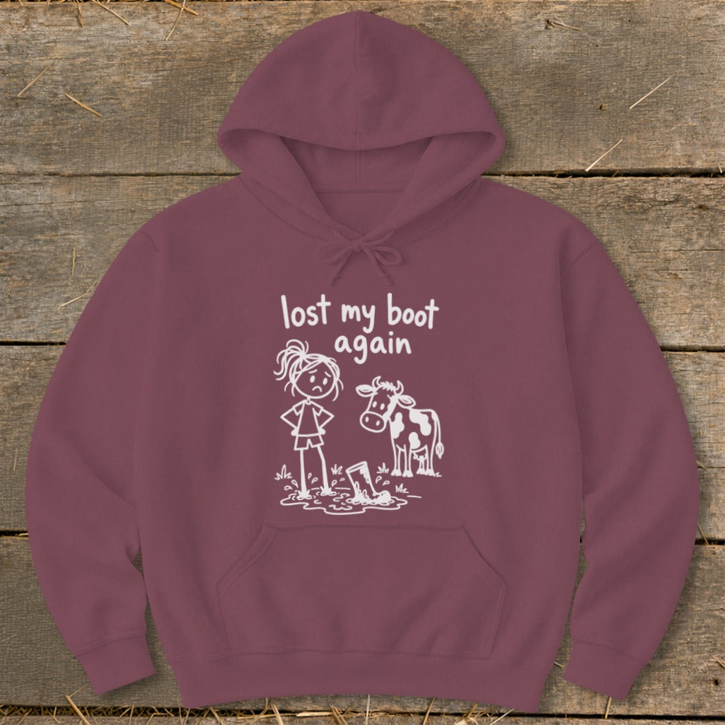 Maroon hoodie featuring a graphic of a frustrated stick-figure girl standing in mud next to a cow, with the text "lost my boot again."
