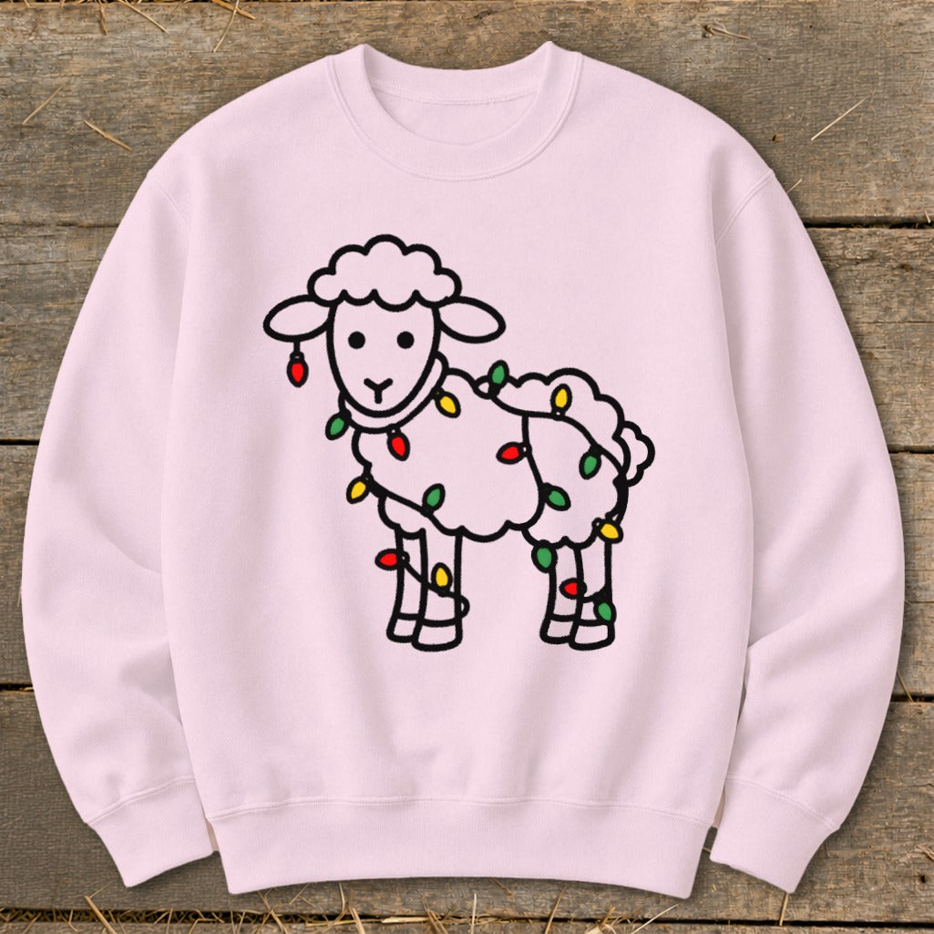 A light pink crewneck sweatshirt features a black outline graphic of a fluffy sheep tangled in colorful Christmas lights.